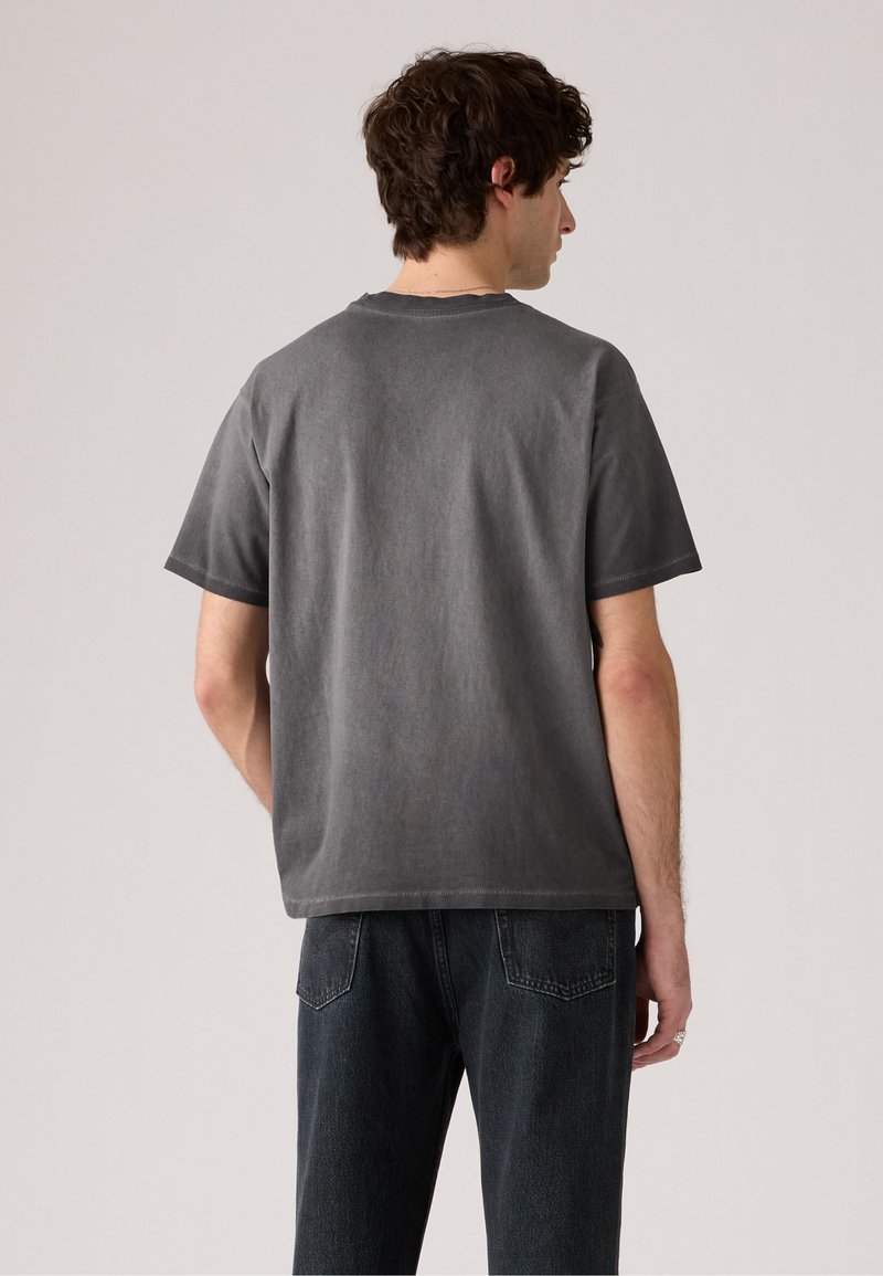 T-shirt en coton gris foncé avec un col rond, des manches courtes et une coupe décontractée. Le tissu a une texture douce et légèrement usée.
