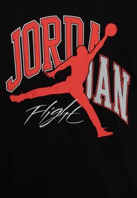 Červená silueta basketbalisty skákajícího s míčem, nad slovem "JORDAN" napsaným tučnými červenými a bílými písmeny s "Flight" napsaným kurzívou níže.