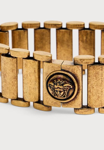 Bracelet à maillons dorés avec un emblème tête de Méduse sur le fermoir, composé de segments rectangulaires et ovales.