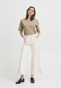 T-shirt beige a maniche corte abbinato a pantaloni bianchi a gamba larga con tasche frontali e orlo pulito, completato da mocassini neri.