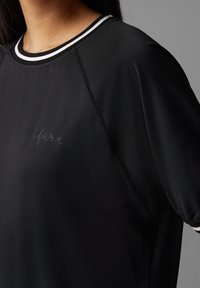 Černé atletické tričko s hladkou strukturou, kulatým výstřihem s bílými akcenty a nápisem "fire" decentně potištěným na látce.