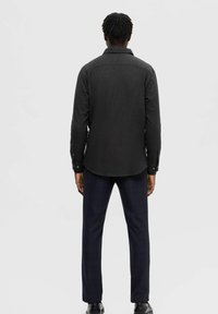 Camisa negra de manga larga con dobladillo curvado y puños con botón, combinada con pantalones en cuadros azul marino. Tejido suave con una textura sutil.