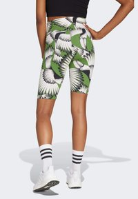 High-waisted green leggings featuring a black and white wing pattern, made of stretchy material, with a smooth texture and fitted design.