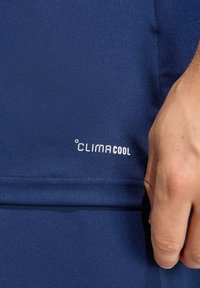 Αθλητικό ύφασμα σε ναυτικό μπλε με ομαλή υφή. Φέρει το λογότυπο ClimaCool σε λευκό, κοντά στη μέση, που τονίζει τον σχεδιασμό που απομακρύνει την υγρασία.