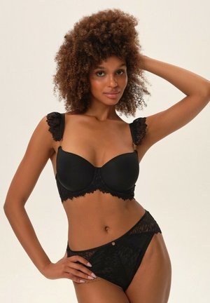 Black bra with lace trim and ruffled straps, featuring a smooth cup design. Accompanied by matching black lace briefs with a small accent.