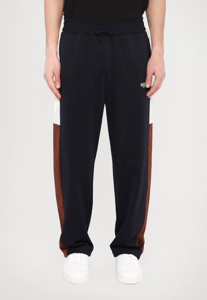 Marineblå sweatpants med hvide og brune sidelister, elastisk talje, snøre og en lille grøn logo detalje, lavet af blødt stof.
