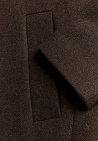 Bruine wollen jasstof met een gestructureerde afwerking. Voorzien van een sierzak en een detail van een omgeslagen mouw. Rijke, diepe kleurtoon.