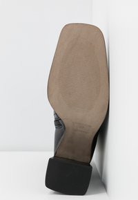 Chaussure à talon noire avec une tige en tissu lisse, un talon bloc, une semelle extérieure en caoutchouc et un motif texturé sur la semelle, montrant des détails et des coutures soignés.