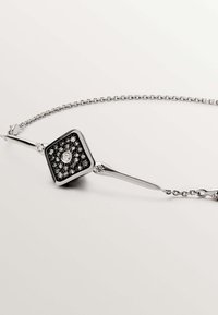Pulsera de plata con un colgante cuadrado adornado con piedras negras y una gema clara en el centro, con un diseño de eslabones de cadena delicados.