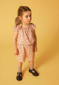 Blumenmuster-Kurzset in Orange und Lavendel mit elastischem Bund. Kombiniert mit dunklen Schuhen und knielangen beigen Socken.