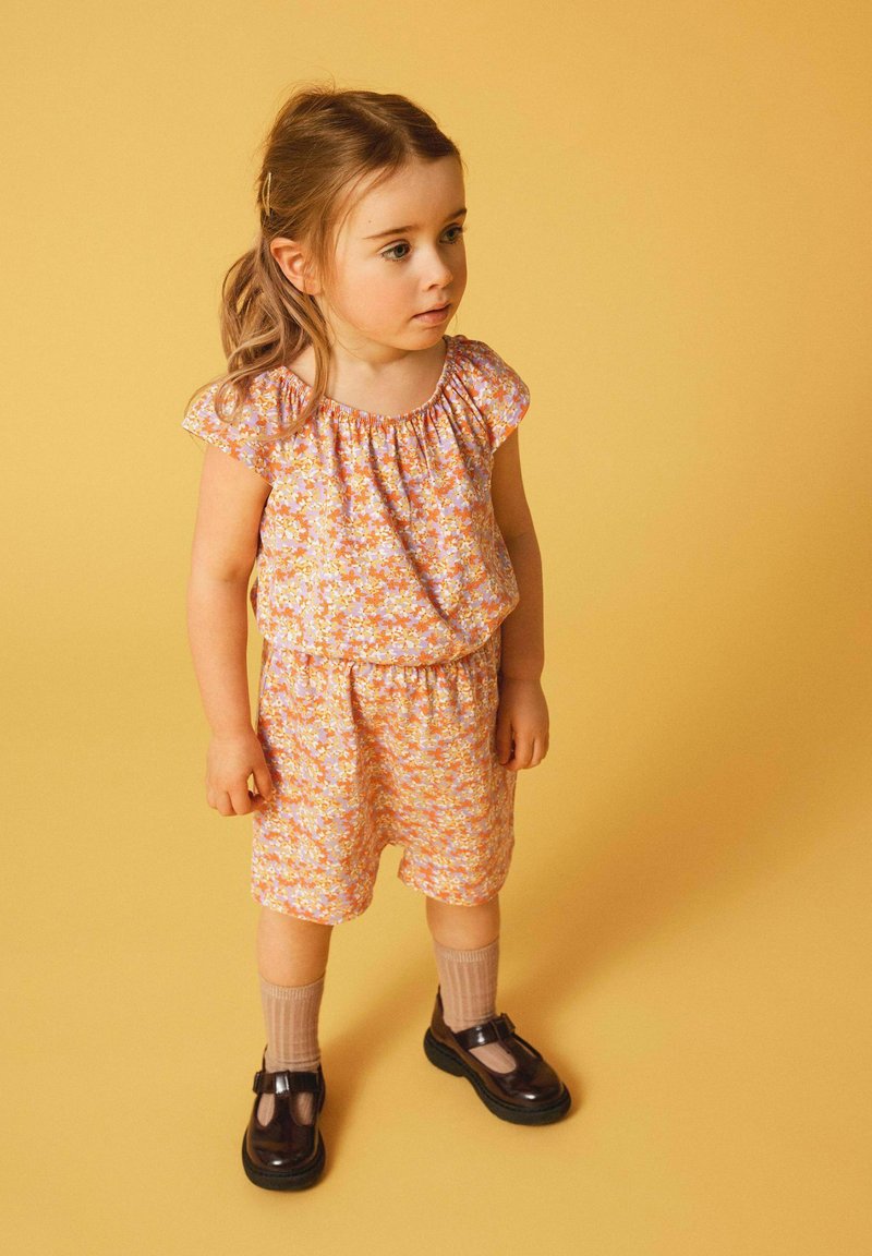 Blumenmuster-Kurzset in Orange und Lavendel mit elastischem Bund. Kombiniert mit dunklen Schuhen und knielangen beigen Socken.