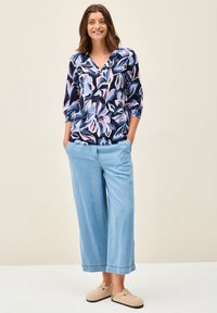 Blusa multicolore in navy con motivo floreale, caratterizzata da scollatura a V e maniche a tre quarti. Pantaloni in denim a gamba larga di un blu chiaro. Scarpe beige da infilare.