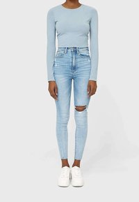 Top de manga larga azul claro combinado con vaqueros pitillo de lavado claro y cintura alta con roturas en las rodillas, complementado con zapatillas blancas.