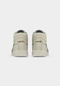 Une paire de baskets hautes Diadora beiges vues de l'arrière sur un fond blanc.