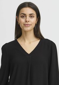 Blusa nera con scollatura a V, tessuto testurizzato, maniche lunghe con leggera arricciatura sulle spalle e una vestibilità rilassata.
