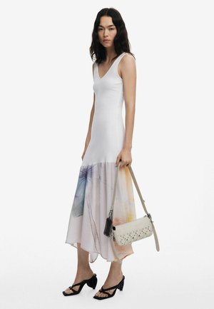 Bijela rebrasta haljina bez rukava sa gradijentnim rubom koji prikazuje cvjetni uzorak u pastelnim bojama. Uparena s bež torbicom preko tijela i crnim sandalama na visoku petu.