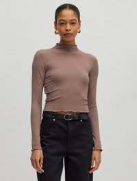 Braun gestreiftes Longsleeve-Oberteil mit hohem Kragen und verkürztem Design, kombiniert mit hoch taillierten schwarzen Hosen und einem schwarzen Gürtel. Strukturierter Stoff.