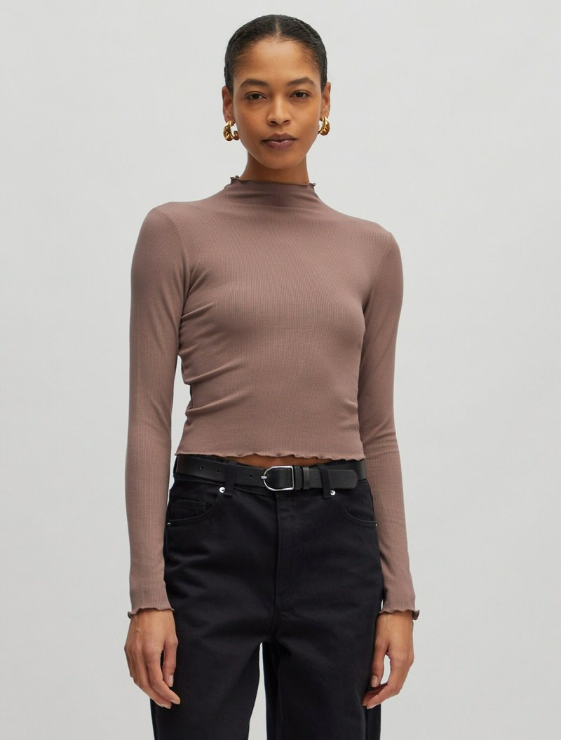 Braun gestreiftes Longsleeve-Oberteil mit hohem Kragen und verkürztem Design, kombiniert mit hoch taillierten schwarzen Hosen und einem schwarzen Gürtel. Strukturierter Stoff.