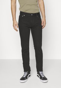 Jeans de mezclilla negros con corte slim, que presentan un clásico diseño de cinco bolsillos y sutiles detalles metálicos. Combinados con zapatillas de deporte altas negras.