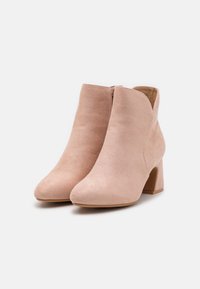 Lyse rosa semskede ankelstøvler med spiss tå og tykk hæl, med en glidelås på siden og en glatt tekstur.