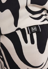 Tkanina w czarno-białe wzory z abstrakcyjnymi kształtami; widoczna metka z logo "M". Tekstura wydaje się gładka i miękka.