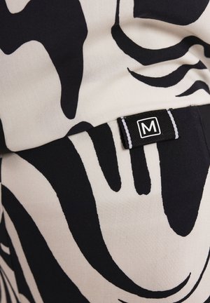 Tkanina w czarno-białe wzory z abstrakcyjnymi kształtami; widoczna metka z logo "M". Tekstura wydaje się gładka i miękka.