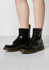 Musta kiiltävä nahka lace-up nilkkurit keltaisilla ompeleilla ja keltaisella vetotaidolla. Ominaisuuksina pyöreä kärki ja teksturoitu kumipohja.