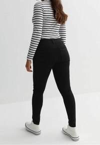 Jeans ajustados negros con una cintura de altura media, que cuentan con bolsillos traseros y un ajuste elegante, combinados con una camiseta de manga larga a rayas y zapatillas blancas.