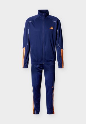 Športni trenirka temno modre barve z jakno z zadrgo po celotni dolžini in ujemajočimi hlačami, ki imata oranžne črte na rokavih in nogah ter oranžni logotip na prsih in stegnih.