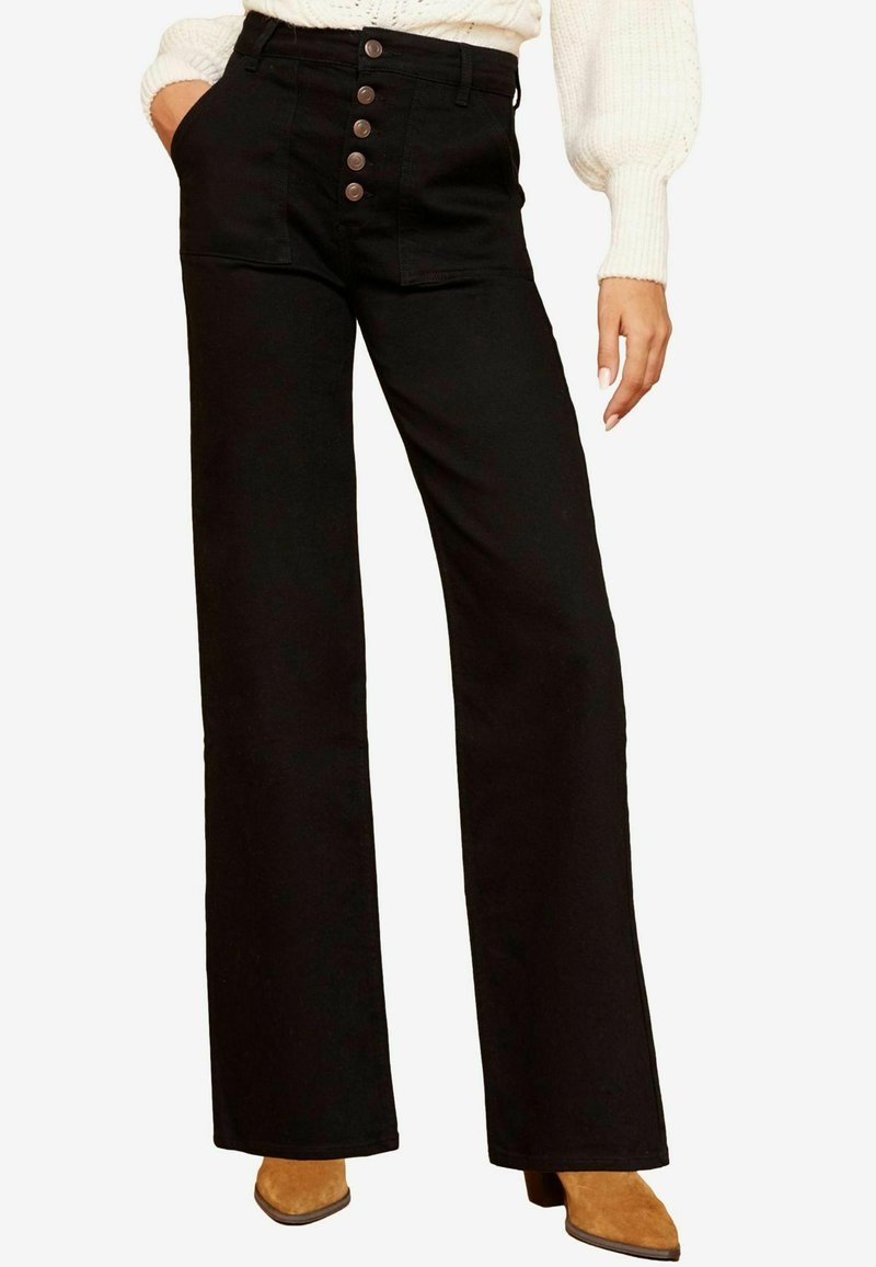 Pantalones negros de pierna ancha hechos de mezclilla, con cintura alta, cierre de cinco botones y bolsillos frontales. La tela parece suave y rígida.