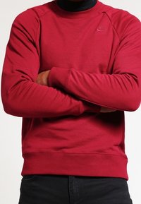 Röd bomullströja med ribbad krage, ribbade ärmslut och midja. Har en liten Nike-logotyp på vänster bröst.