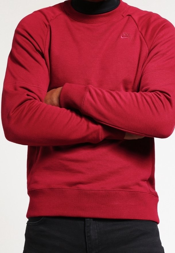 Röd bomullströja med ribbad krage, ribbade ärmslut och midja. Har en liten Nike-logotyp på vänster bröst.