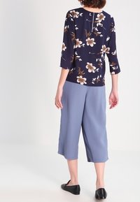 Navy floral blouse with three-quarter sleeves, paired with light blue culottes. Smooth texture, featuring a back keyhole detail. Black flat shoes.