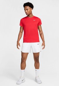 Punane lühikeste varrukatega sportlik T-särk Nike logoga; sellega on kaasas valged lühikesed püksid küljetaskutega ja peene disainiga, mida täiustavad valged sokid ja kingad.