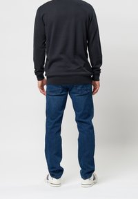 Mörkgrå stickad tröja med ribbade muddar och nederkant, tillsammans med blå denimjeans med bakfickor och en rak passform. Vita sneakers ingår.