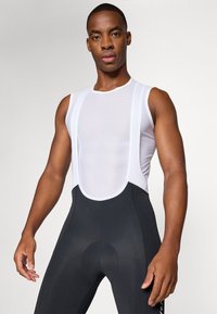 Cuissards de cyclisme noirs avec une assise rembourrée, dotés d'un haut en maille blanche respirante et de larges bretelles. Texture lisse avec des coutures surpiquées.