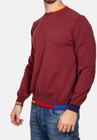 Bordeaux gebreide sweater met een ronde hals, voorzien van kleurrijke gestreepte accenten bij de kraag en de zoom. Lange mouwen met geribbelde manchetten.