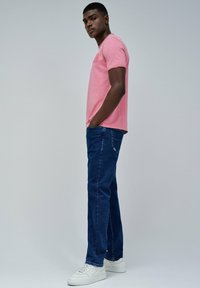 Camiseta de algodón rosa, jeans de mezclilla azul y zapatillas blancas. La camiseta tiene un cuello redondo y mangas cortas; los jeans tienen un corte estándar.