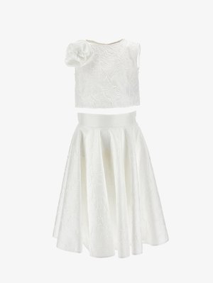 Fehér, két részes ruházat texturált anyagból, ujjatlan crop top nagy virág díszítéssel az egyik vállon, és magas derekú, bővülő szoknyával.