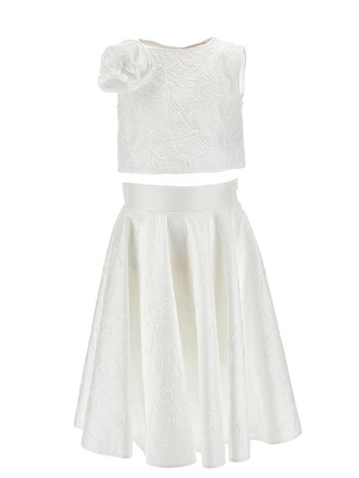 Hvid todelt sæt i tekstureret stof, bestående af en ærmeløs crop-top med en stor blomst på den ene skulder og en højttaljet, udvidet nederdel.