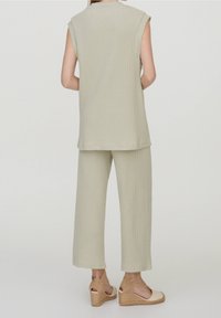 Mujer vistiendo una blusa sin mangas de canalé beige claro y pantalones de pierna ancha con sandalias de cuña beige, de pie contra un fondo liso.