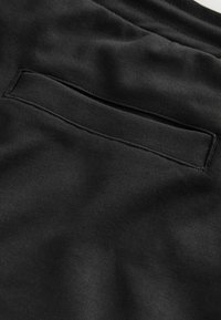 Mustast kangast tasku lähedalt, millel on horisontaalne ava ja nähtavad õmblused sileda tekstiilipinna peal.