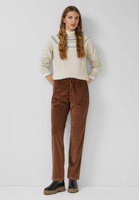 Beżowy sweter z wzorzystym detalem przy dekolcie, zestawiony z brązowymi sztruksowymi spodniami. Czarne botki na masywnych podeszwach dopełniają stylizację.