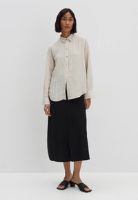 Camicia a maniche lunghe di un bianco sporco con tessuto texturizzato, abbinata a una gonna midi nera e sandali neri scivolati.