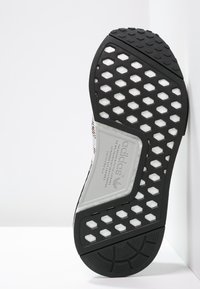 Sole of Adidas sneaker showing black outsole with hexagonal cutouts revealing white midsole and Adidas branding in the arch area.