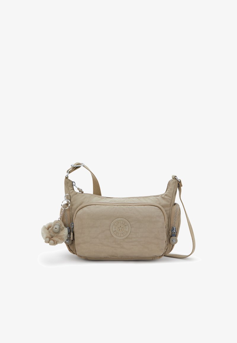 Sac bandoulière beige avec une finition texturée, doté d'un compartiment principal zippé, d'une sangle ajustable et d'un porte-clés en peluche attaché.