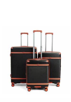 Set di tre valigie rigide nere con rifiniture marroni, manici telescopici estesi e quattro ruote arancioni su ciascuna.
