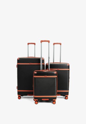 Set di tre valigie rigide nere con rifiniture marroni, manici telescopici estesi e quattro ruote arancioni su ciascuna.