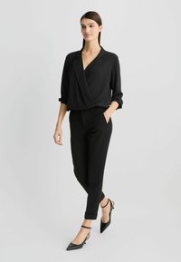 Čierna blúzka s dlhými rukávmi, doplnená čiernymi upravenými nohavicami. Oblečenie má elegantný, minimalistický dizajn a štruktúrovaný strih.