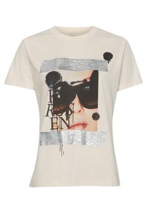 Beżowa koszulka z grafiką twarzy kobiety w ciemnych okularach przeciwsłonecznych, pokrytą czarnymi plamami farby, literami oraz srebrnymi metalicznymi paskami.